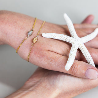 A picture of &Lottie Yemaja bracelets, featuring a cowrie shell chain bracelet available in yellow gold and yellow gold and silver.