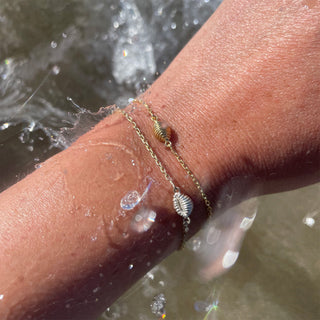 A picture of &Lottie Yemaja bracelets, featuring a cowrie shell chain bracelet available in yellow gold and yellow gold and silver.